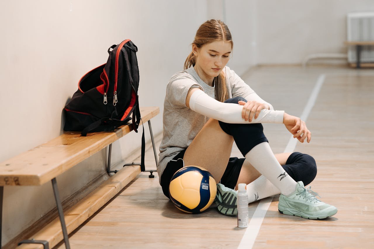 A woman volleyball player in sportswear, sitting on an indoor court bench with equipment.